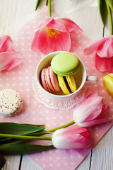 A beautiful flowers pink tulips with colorful macaroons laid in cup on white wooden background