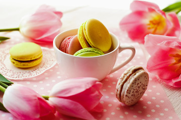 A beautiful flowers pink tulips with colorful macaroons laid in cup on white wooden background