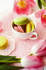 A beautiful flowers pink tulips with colorful macaroons laid in cup on white wooden background
