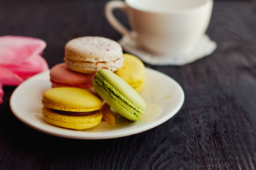 A beautiful flowers pink tulips with colorful macaroons laid on a white platter on dark wooden background