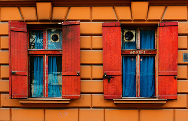 Fototapeta na wymiar two old windows with red shutters in the stone wall with blue curtains