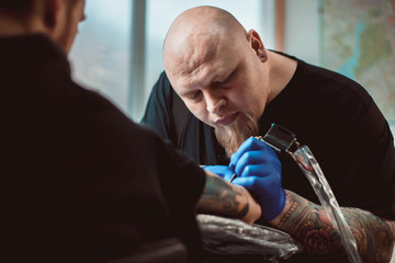 master tattoo artist with a beard makes gloves tattoo on hand men