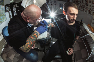 master tattooist makes a tattoo on the skin of the client in a workshop with special equipment