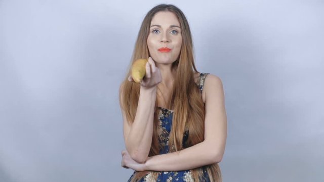 Beautiful young girl eating a pear in studio. Young healthy young woman holding up a fresh pear and eating. Concept of healthy eating, dieting and nutrition.