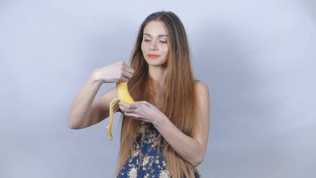 Cute blonde woman wearing floral dress peeling and biting a banana.