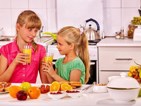 Children drinking orange fresh at kitchen. Mom pours juice daughter.