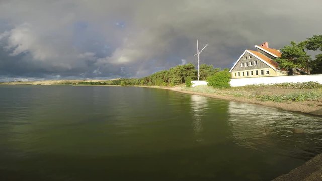 Rainbow over the house against black cloudy sky shot from cement pier, 4K