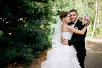 Elegant young happy wedding couple is sitting at green grass on