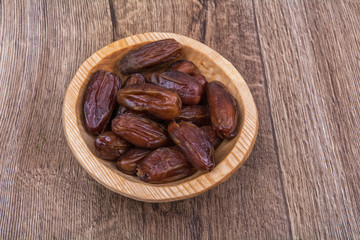 Dried dates in a wooden bowl on a wooden background