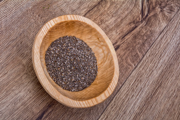 Chia seeds in a wooden bowl on a wooden background