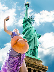 A smiling and fashionable woman with a orange wide-brimmed hat takes a selfie. Statue of Liberty...