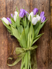 bouquet of white and purple tulips with green ribbon on wood