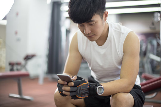 Young Handsome Asian Man Using Smart Phone In Modern Gym