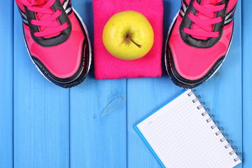 Pair of sport shoes and fresh apple on blue boards, copy space for text on sheet of paper