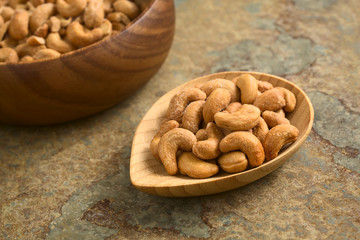 Fototapeta na wymiar Salted cashew nuts or seeds on small bamboo plate, photographed on slate with natural light (Selective Focus, Focus on the first cashews on the plate)