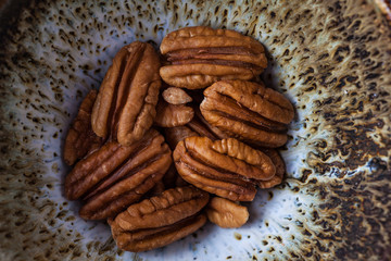 Pecans in handmade ceramic bowl extreme closeup, top view.
