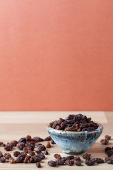 Organic raisins in handmade ceramic bowl on wooden table. Vertical image with copy space. Shallow depth of field.
