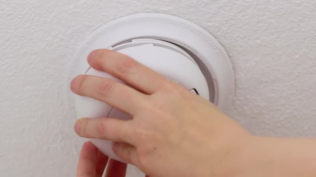 Low angle view of a hand installing a smoke detector and alarm in a ceiling in the USA.  Finger then presses button to test alarm.  Originally recorded in 4K