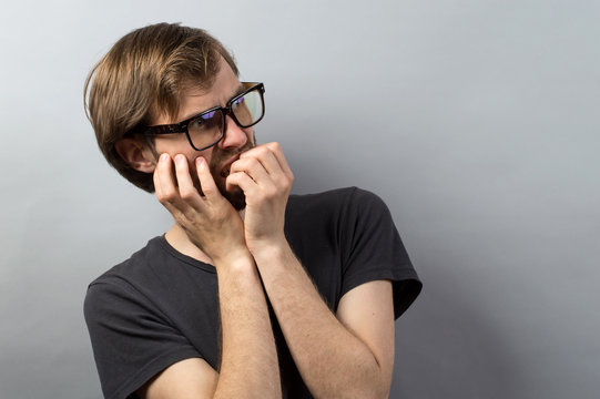 young man biting his nails on a light gray studio background