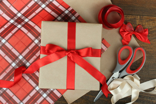 beautiful packaging for gift with red ribbon and scissors on wooden background