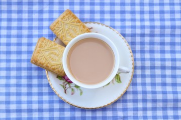 Traditional milky tea served in a bone china cup and saucer with custard cream type biscuits