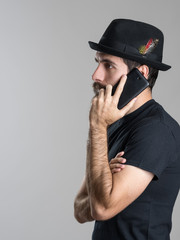 Side view of pensive bearded young man talking on the phone looking away over gray studio background
