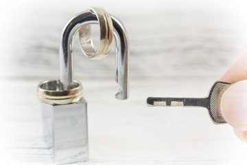 Obraz premium Wedding rings on opened shiny padlock and hand holding key. Concept for marriage problems