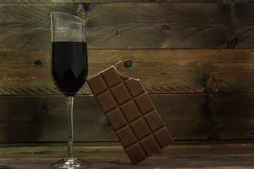 Red wine glass and bitten chocolate bar on vintage wooden background. Concept for unhealthy food and life style