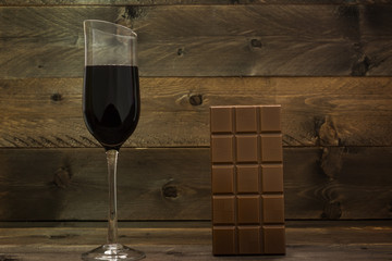 Red wine glass and chocolate bar on vintage wooden background