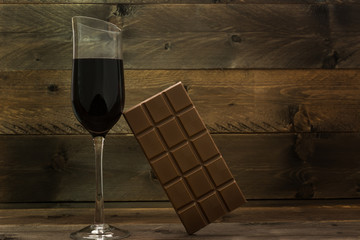 Red wine glass and chocolate bar on vintage wooden background - obrazy, fototapety, plakaty