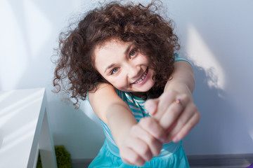 Fototapeta premium Portrait of a beautiful young girl with brown curly hair. Fun and joy. Happy girl in the morning sun is smiling at the camera. Delicate blue dress.