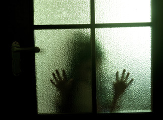 Blurred silhouette of a child behind a glass door in the darkness (symbolizing sadness, loneliness, horror or fear)