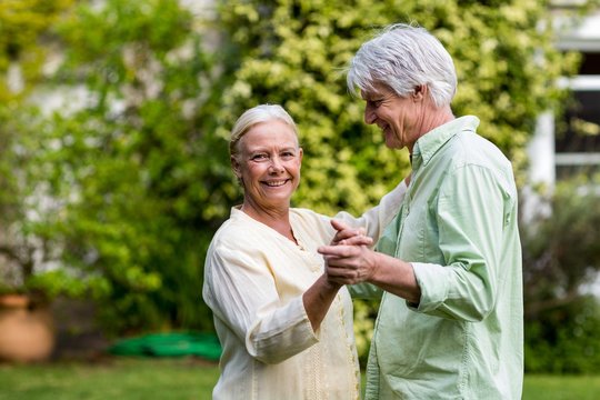 Smiling Senior Woman With Man Dancing In Yard