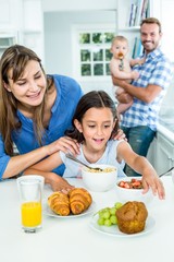Woman looking at daughter having breakfast in kitchen