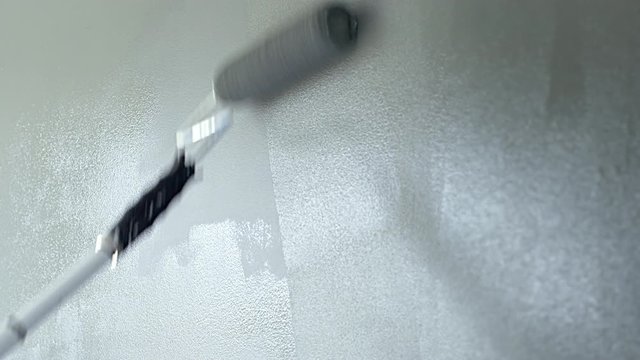 Gray paint being applied to a wall with a roller brush on an extension arm.  Wet paint around patch being painted. Originally recorded in 4K.