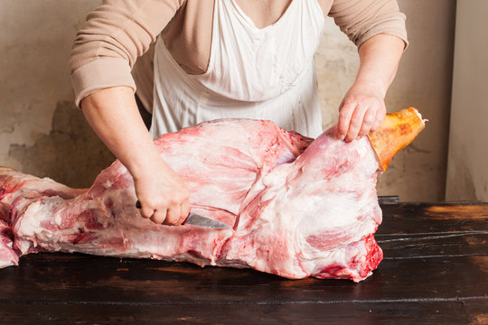 Butcher carving raw pork. Butcher carving carcass of raw pork. Butcher carving raw pork on wooden table. 
