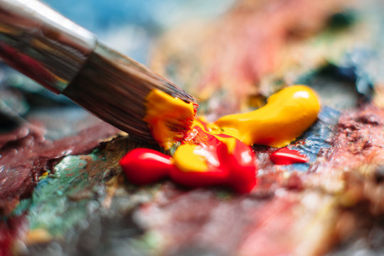 Painter mixes yellow and red oil paint on the palette. Closeup of paint mixing process in art workplace.