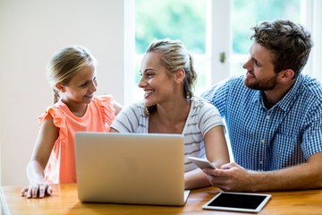Smiling parents with technologies looking at daughter in house 