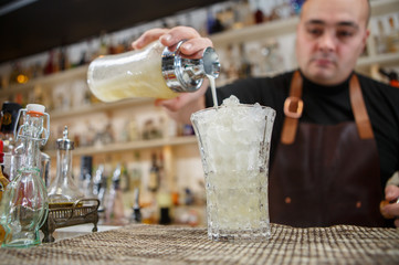 Bartender pouring cocktail into glass at the bar