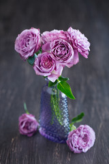 Beautiful fresh purple roses in a vase on a dark brown wooden background .