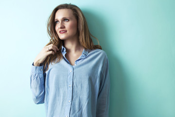 Obraz premium Bright young blond girl is smiling and posing against the cyan wall