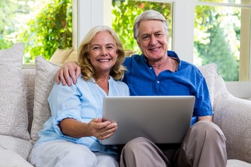 Fototapeta premium Senior couple holding laptop while sitting on sofa at home
