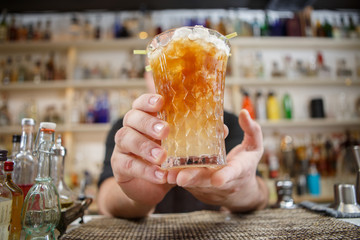 Bartender is standing in pubб holding cocktail and giving glass forward. Focus on beverage.