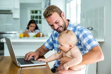 Obraz premium Father looking at baby boy while using laptop at home