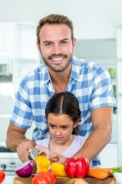 Father assisting daughter in cutting vegetables at home