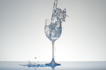 Water with blue tint pouring into a wineglass with splashes.