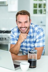 Happy man leaning by laptop at table in kitchen