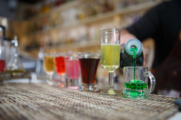 Bartender pours various of alcohol drink into small glasses on bar