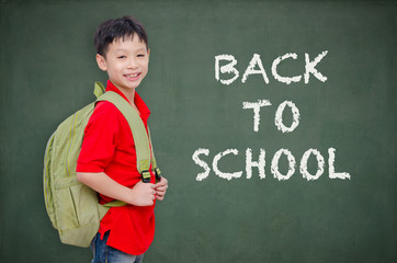 Young Asian schoolboy with backpack standing in front of chalkbo