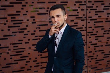 Portrait of a young businessman smoking cigarette outside the of